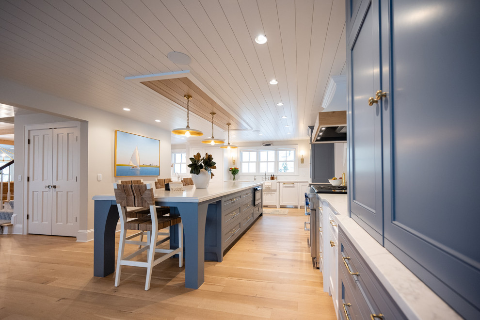 Beach style l-shaped separate kitchen in Minneapolis with a farmhouse sink, beaded inset cabinets, blue cabinets, solid surface benchtops, white splashback, stone tile splashback, panelled appliances, light hardwood floors, with island, white benchtop and timber.