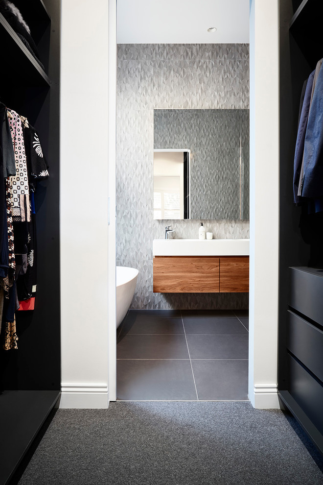Photo of a mid-sized contemporary master bathroom in Melbourne with flat-panel cabinets, medium wood cabinets, a freestanding tub, an open shower, a one-piece toilet, gray tile, porcelain tile, grey walls, porcelain floors, an integrated sink, solid surface benchtops, grey floor, an open shower and white benchtops.
