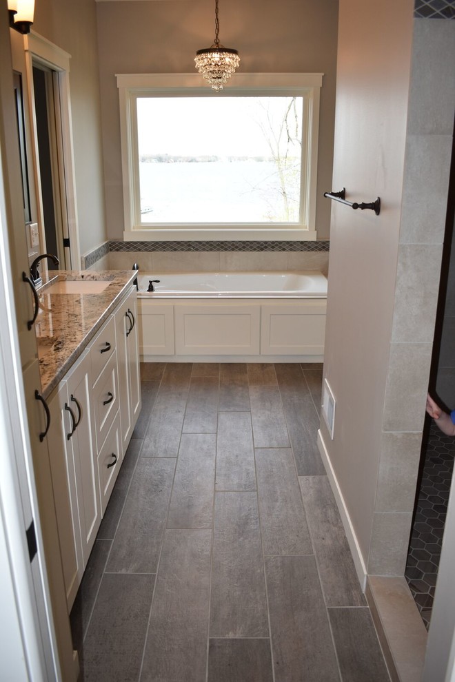 Drop-in bathtub - mid-sized traditional master beige tile and ceramic tile porcelain tile and brown floor drop-in bathtub idea in Minneapolis with shaker cabinets, white cabinets, a two-piece toilet, gray walls, an undermount sink and granite countertops