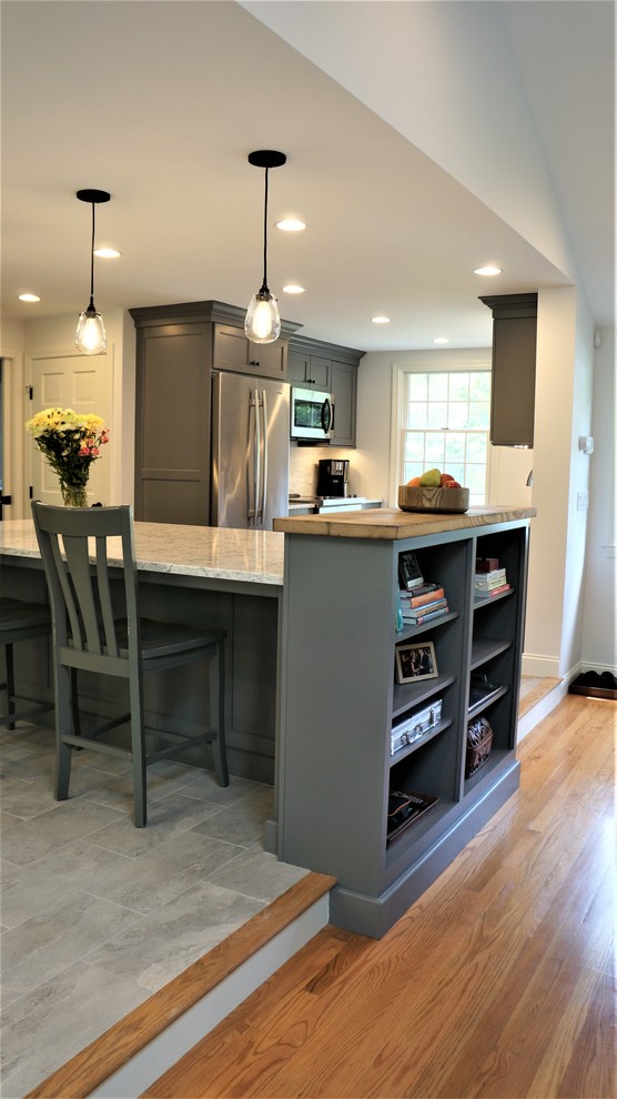 Mid-sized transitional galley porcelain tile and gray floor open concept kitchen photo in Boston with a farmhouse sink, recessed-panel cabinets, quartz countertops, white backsplash, porcelain backsplash, stainless steel appliances, an island and white countertops
