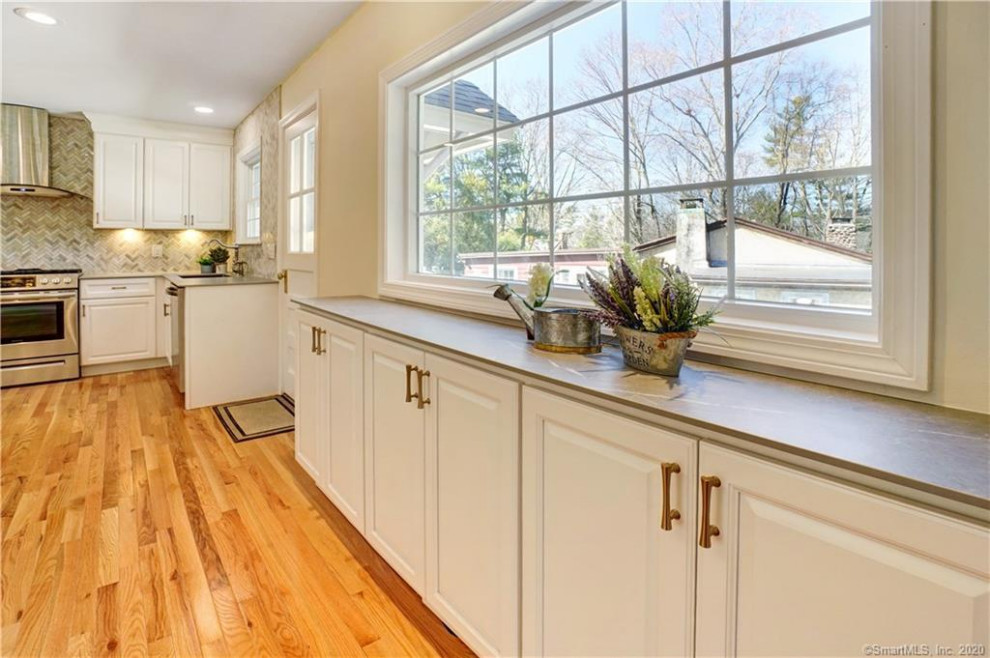 Mid-sized transitional l-shaped light wood floor eat-in kitchen photo with an undermount sink, shaker cabinets, white cabinets, marble backsplash, stainless steel appliances and gray countertops