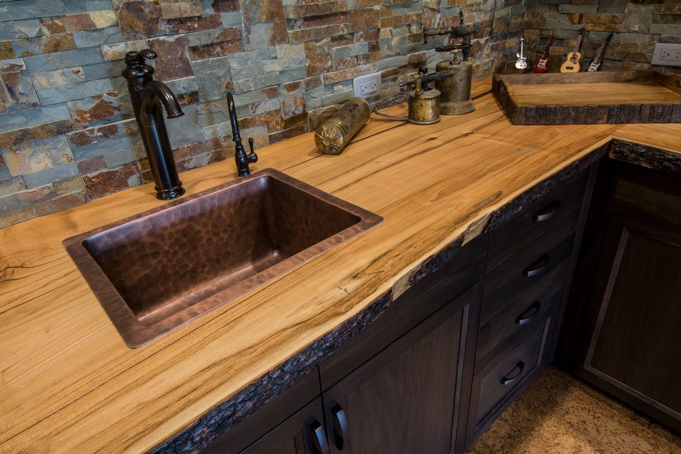 Design ideas for a mid-sized country u-shaped wet bar in Calgary with recessed-panel cabinets, dark wood cabinets, wood benchtops, stone tile splashback, brown splashback, brown floor, brown benchtop and a drop-in sink.