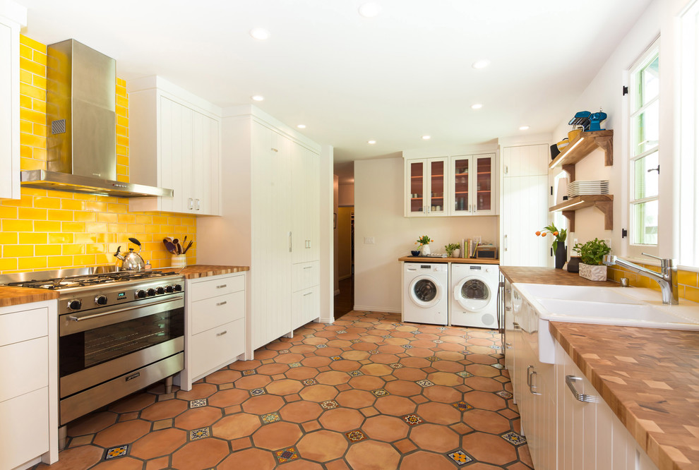 Design ideas for a mediterranean u-shaped kitchen in Los Angeles with a drop-in sink, flat-panel cabinets, white cabinets, yellow splashback, subway tile splashback, stainless steel appliances, terra-cotta floors and no island.
