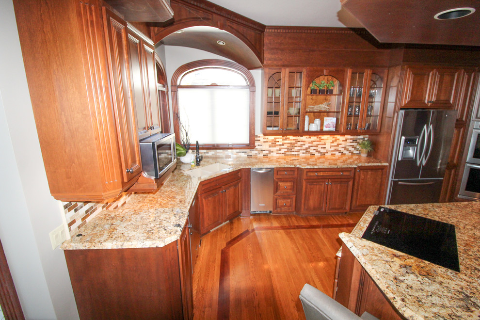 Inspiration for a medium tone wood floor and brown floor kitchen remodel with an undermount sink, raised-panel cabinets, dark wood cabinets, granite countertops, multicolored backsplash, ceramic backsplash, stainless steel appliances, an island and orange countertops