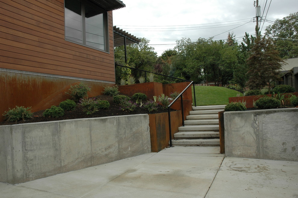 This is an example of a large modern front yard full sun xeriscape for summer in Salt Lake City with a retaining wall and concrete pavers.