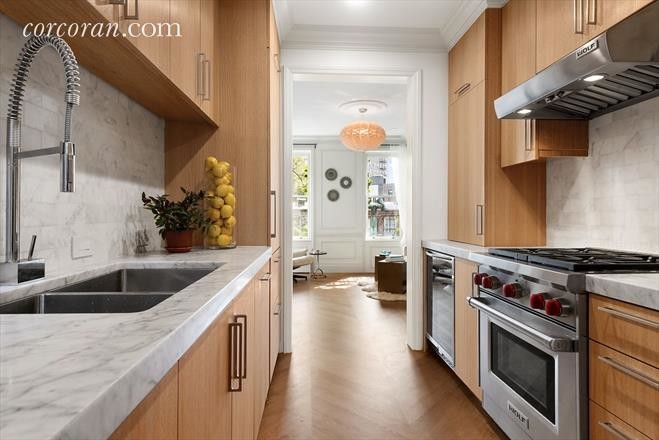 This is an example of a mid-sized transitional galley eat-in kitchen in New York with a double-bowl sink, flat-panel cabinets, light wood cabinets, granite benchtops, white splashback, stone tile splashback, stainless steel appliances, light hardwood floors and no island.