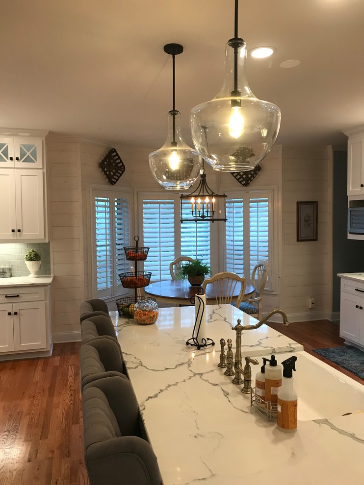 Example of a mid-sized transitional u-shaped medium tone wood floor and brown floor eat-in kitchen design in Atlanta with a farmhouse sink, shaker cabinets, white cabinets, subway tile backsplash, stainless steel appliances, an island and granite countertops