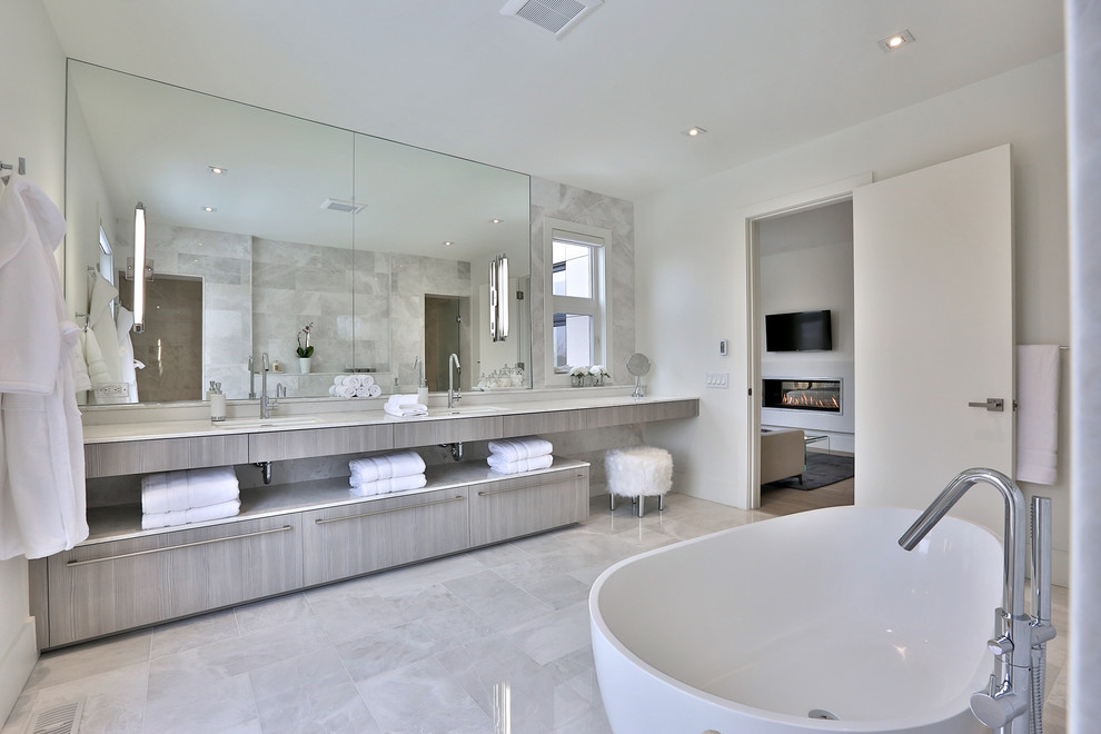 Design ideas for an expansive contemporary master bathroom in Toronto with flat-panel cabinets, light wood cabinets, a freestanding tub, white walls, an undermount sink, gray tile, stone tile, marble floors and marble benchtops.