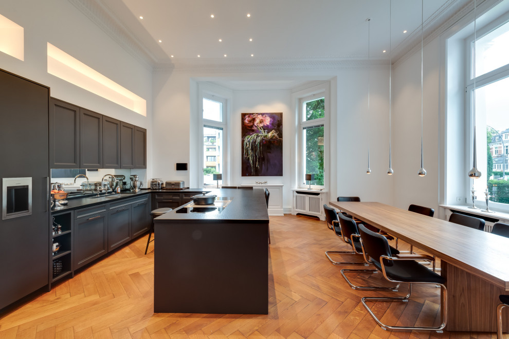 This is an example of an expansive midcentury u-shaped open plan kitchen in Hamburg with a double-bowl sink, beaded inset cabinets, black cabinets, laminate benchtops, white splashback, mirror splashback, black appliances, painted wood floors, a peninsula, brown floor, black benchtop and vaulted.