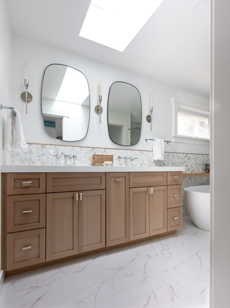 Пример оригинального дизайна: большая главная ванная комната в стиле неоклассика (современная классика) с фасадами с утопленной филенкой, светлыми деревянными фасадами, отдельно стоящей ванной, двойным душем, унитазом-моноблоком, белой плиткой, мраморной плиткой, белыми стенами, полом из керамогранита, врезной раковиной, столешницей из искусственного кварца, белым полом, душем с распашными дверями, белой столешницей, сиденьем для душа, тумбой под две раковины и напольной тумбой