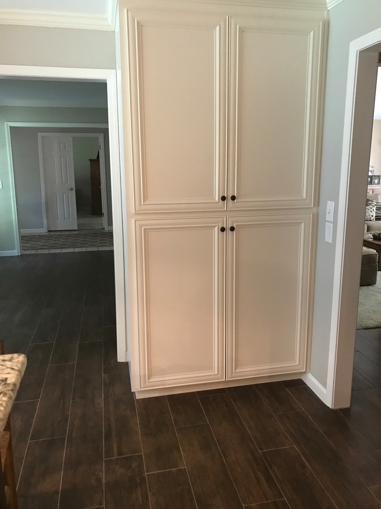 Example of a large transitional l-shaped brown floor eat-in kitchen design in Birmingham with a farmhouse sink, recessed-panel cabinets, white cabinets, beige backsplash, stainless steel appliances and an island