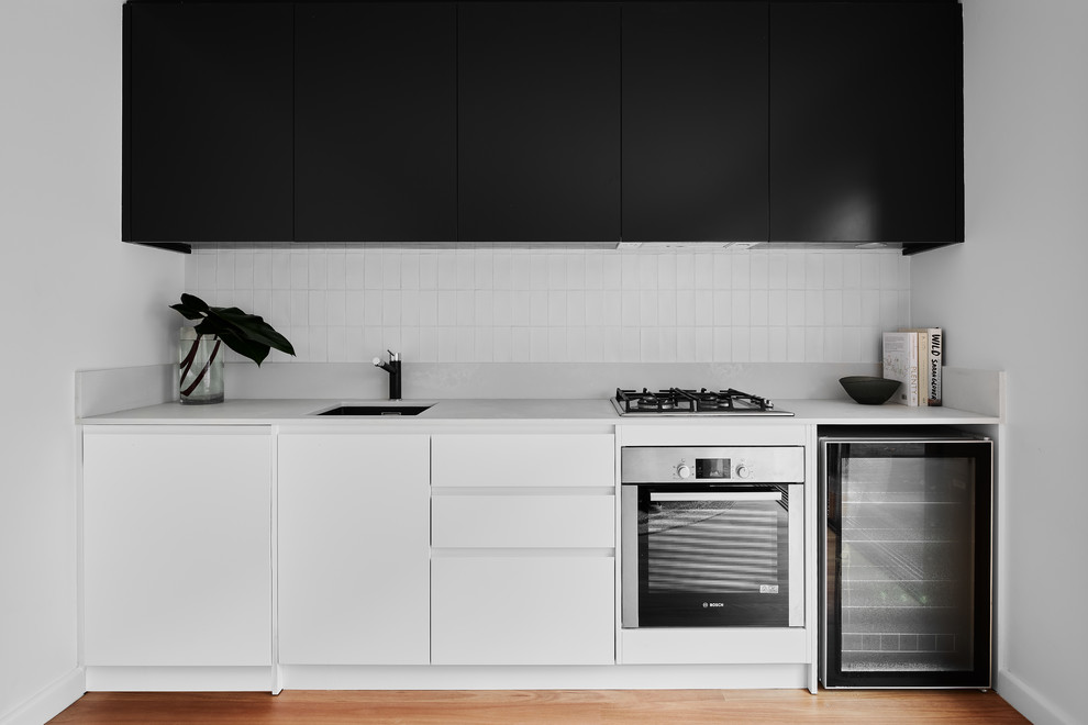 This is an example of a small contemporary single-wall eat-in kitchen in Wollongong with an undermount sink, beaded inset cabinets, black cabinets, quartz benchtops, white splashback, ceramic splashback, stainless steel appliances, light hardwood floors, no island, grey benchtop and brown floor.