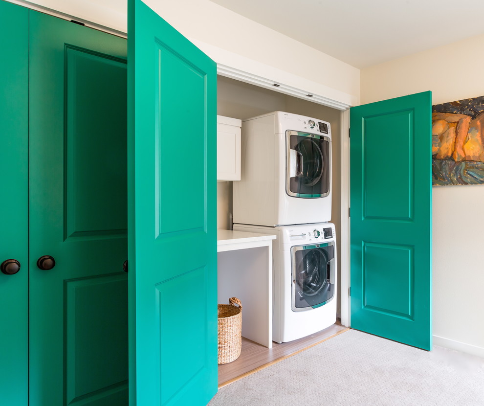 This is an example of a mid-sized transitional laundry cupboard in Seattle with beige walls, carpet and a stacked washer and dryer.