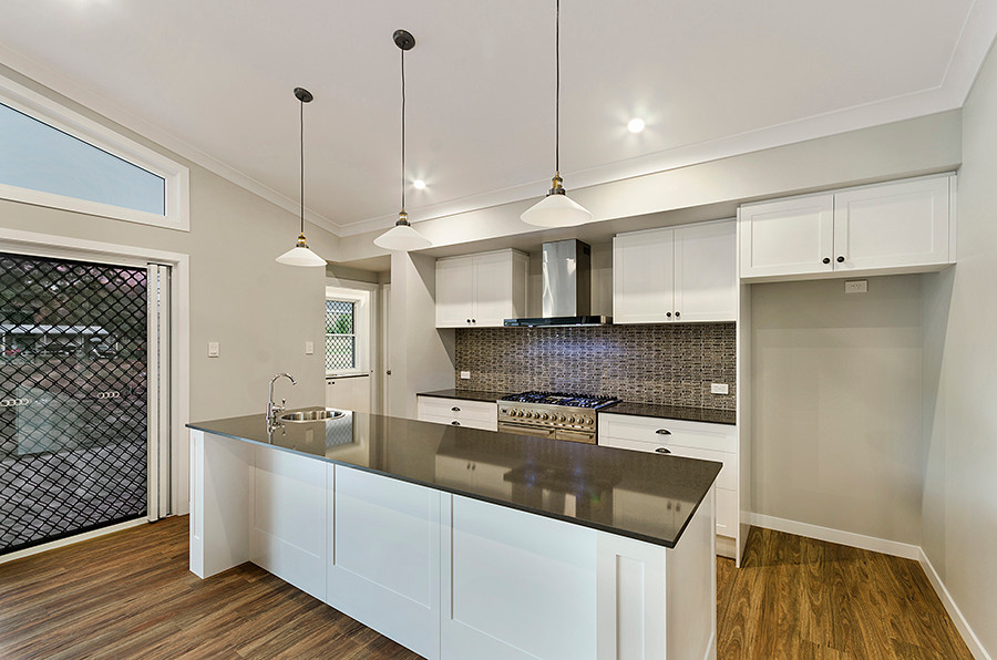 Design ideas for a galley open plan kitchen in Townsville with shaker cabinets, white cabinets, with island, a single-bowl sink, stainless steel appliances, quartz benchtops, porcelain splashback, vinyl floors and brown floor.