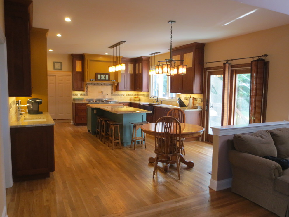 Photo of a large traditional l-shaped eat-in kitchen in New York with a farmhouse sink, shaker cabinets, dark wood cabinets, wood benchtops, beige splashback, stone tile splashback, stainless steel appliances, light hardwood floors and with island.