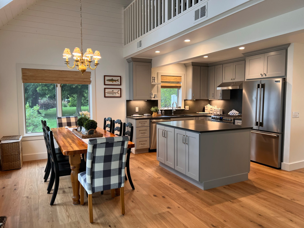 Mid-sized beach style l-shaped light wood floor, brown floor and wood ceiling open concept kitchen photo in Detroit with an undermount sink, shaker cabinets, gray cabinets, quartz countertops, black backsplash, quartz backsplash, stainless steel appliances, an island and black countertops