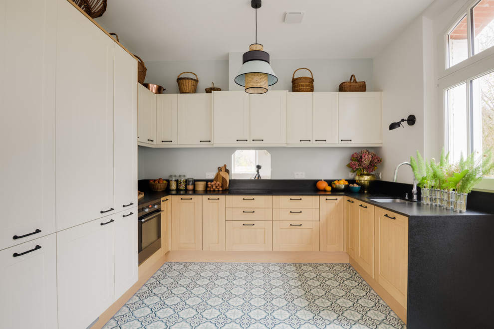 Photo of a transitional l-shaped open plan kitchen in Paris with cement tiles, black benchtop, an undermount sink, shaker cabinets, light wood cabinets, stainless steel appliances, blue floor, granite benchtops and mirror splashback.