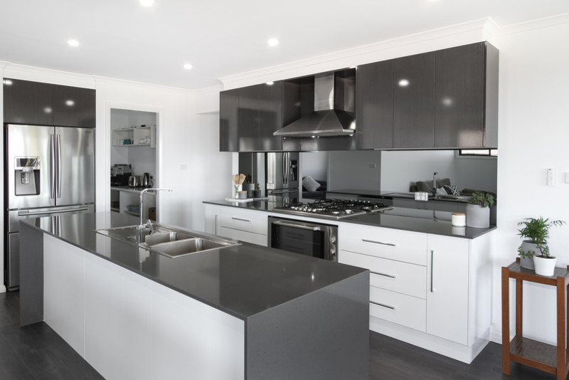 Modern galley open plan kitchen in Newcastle - Maitland with a double-bowl sink, white cabinets, quartz benchtops, mirror splashback, stainless steel appliances, laminate floors, with island, grey floor and grey benchtop.
