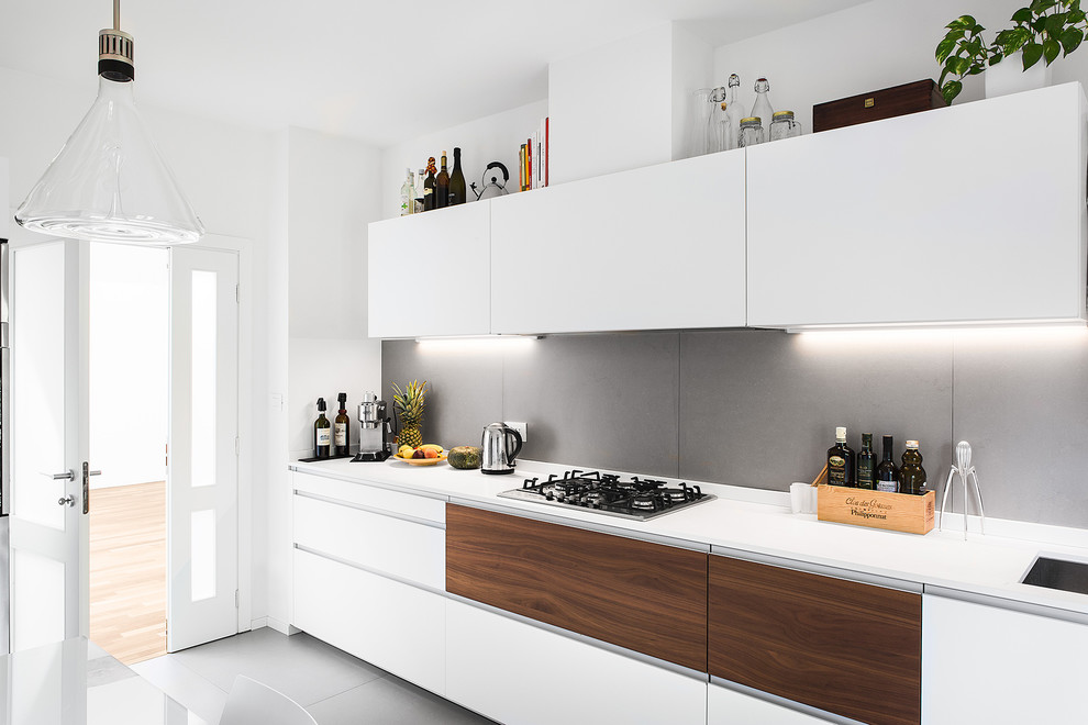 Design ideas for a mid-sized contemporary single-wall separate kitchen in Bologna with a single-bowl sink, flat-panel cabinets, white cabinets, solid surface benchtops, grey splashback, stainless steel appliances, porcelain floors, no island and grey floor.