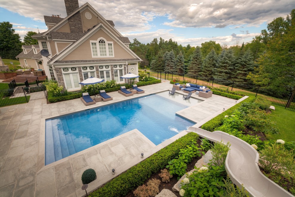 This is an example of a large contemporary side yard rectangular pool in Toronto with a water slide and natural stone pavers.