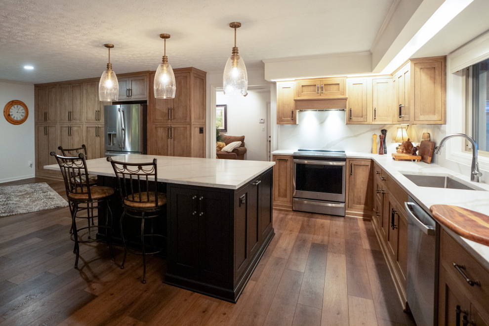 Large transitional l-shaped medium tone wood floor and brown floor eat-in kitchen photo with a single-bowl sink, shaker cabinets, medium tone wood cabinets, quartz countertops, white backsplash, quartz backsplash, stainless steel appliances, an island and white countertops