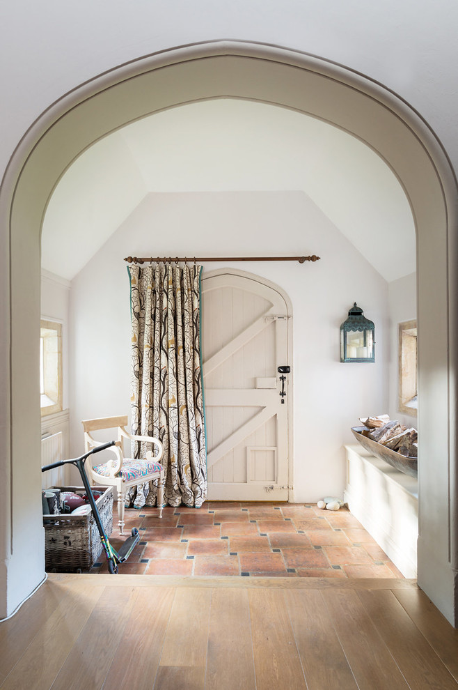 Photo of a country entryway in Hampshire with white walls, terra-cotta floors, a single front door and red floor.