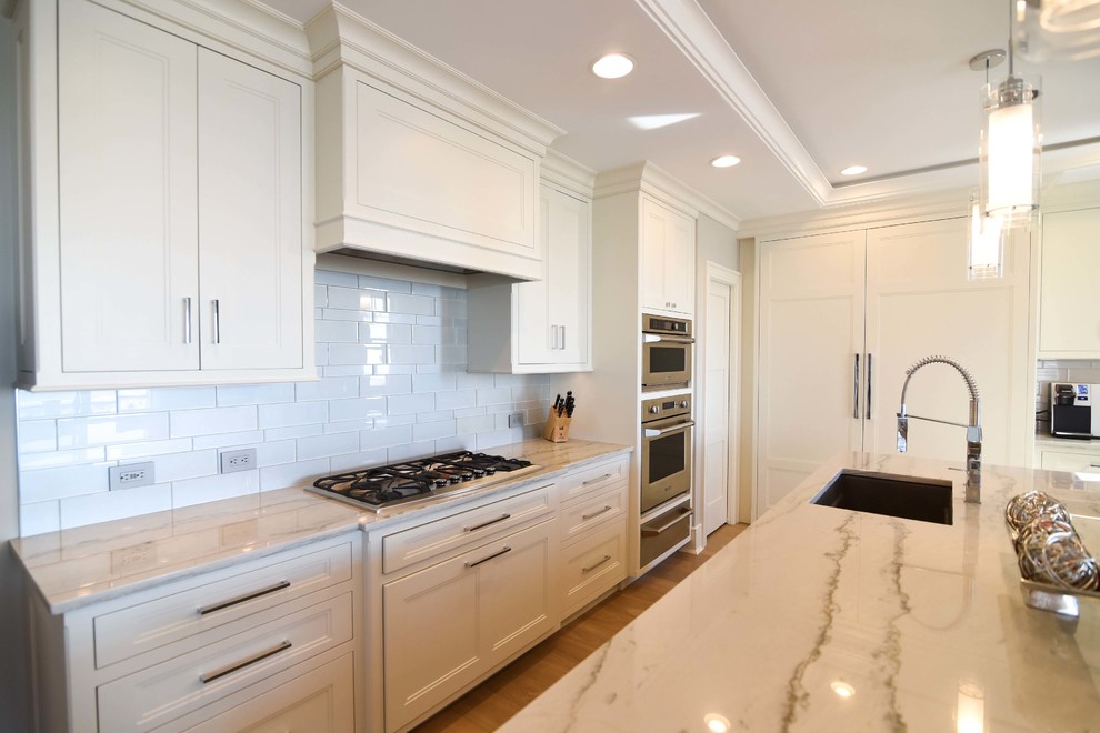 Inspiration for a mid-sized transitional l-shaped open plan kitchen in Philadelphia with an undermount sink, white splashback, panelled appliances, light hardwood floors, with island, brown floor, beaded inset cabinets, beige cabinets, quartzite benchtops, ceramic splashback and white benchtop.