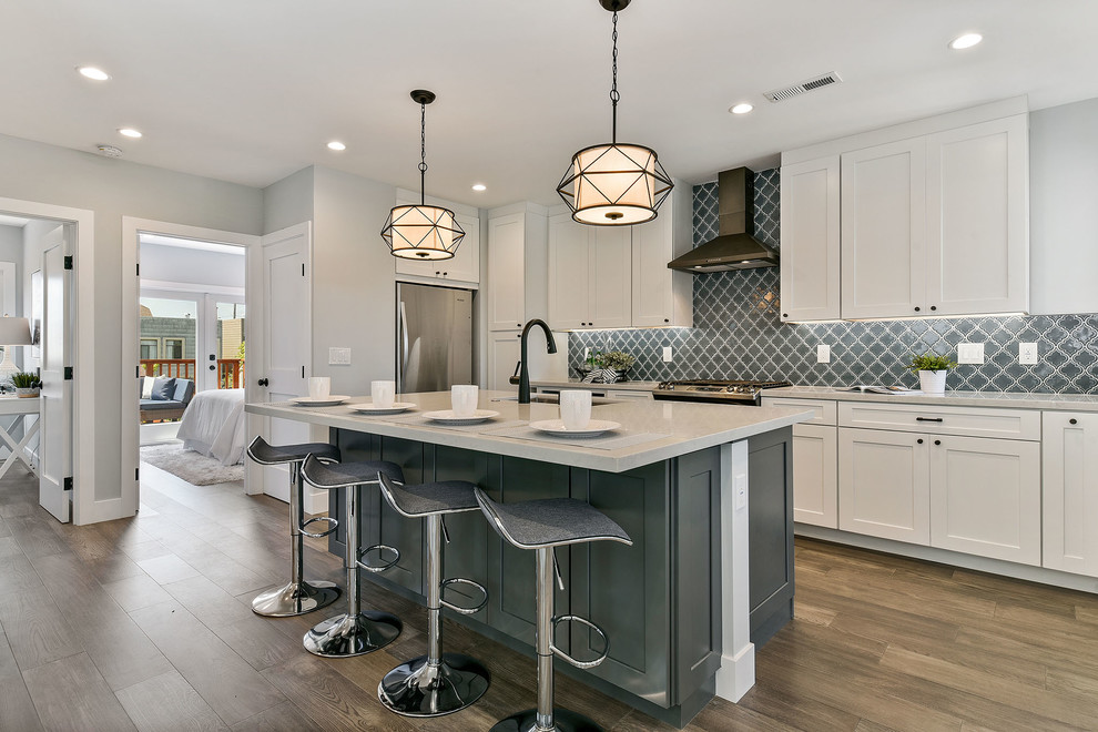 Photo of a mid-sized transitional l-shaped open plan kitchen in San Francisco with an undermount sink, shaker cabinets, white cabinets, quartzite benchtops, grey splashback, porcelain splashback, stainless steel appliances, medium hardwood floors, with island, white benchtop and brown floor.