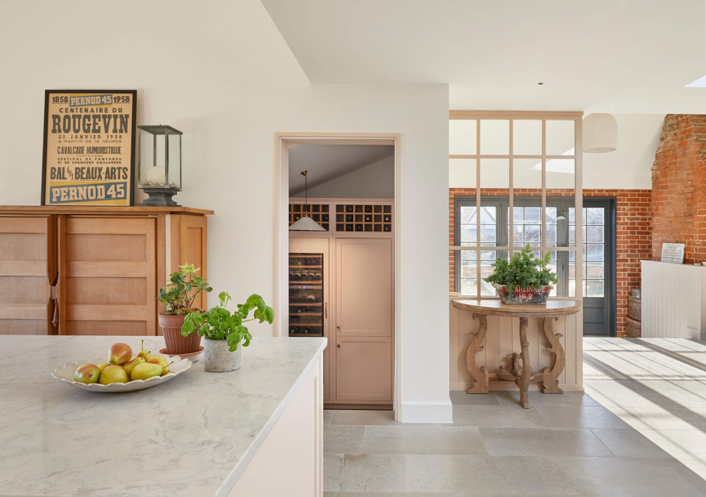 Photo of a large rural grey and pink single-wall open plan kitchen in London with a belfast sink, shaker cabinets, pink cabinets, quartz worktops, pink splashback, black appliances, ceramic flooring, an island, multi-coloured floors, grey worktops and a vaulted ceiling.