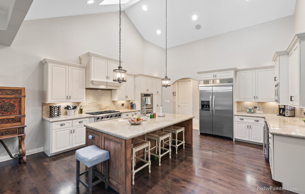 Inspiration for a huge timeless u-shaped dark wood floor, brown floor and vaulted ceiling eat-in kitchen remodel with an undermount sink, raised-panel cabinets, white cabinets, granite countertops, beige backsplash, travertine backsplash, stainless steel appliances, an island and beige countertops
