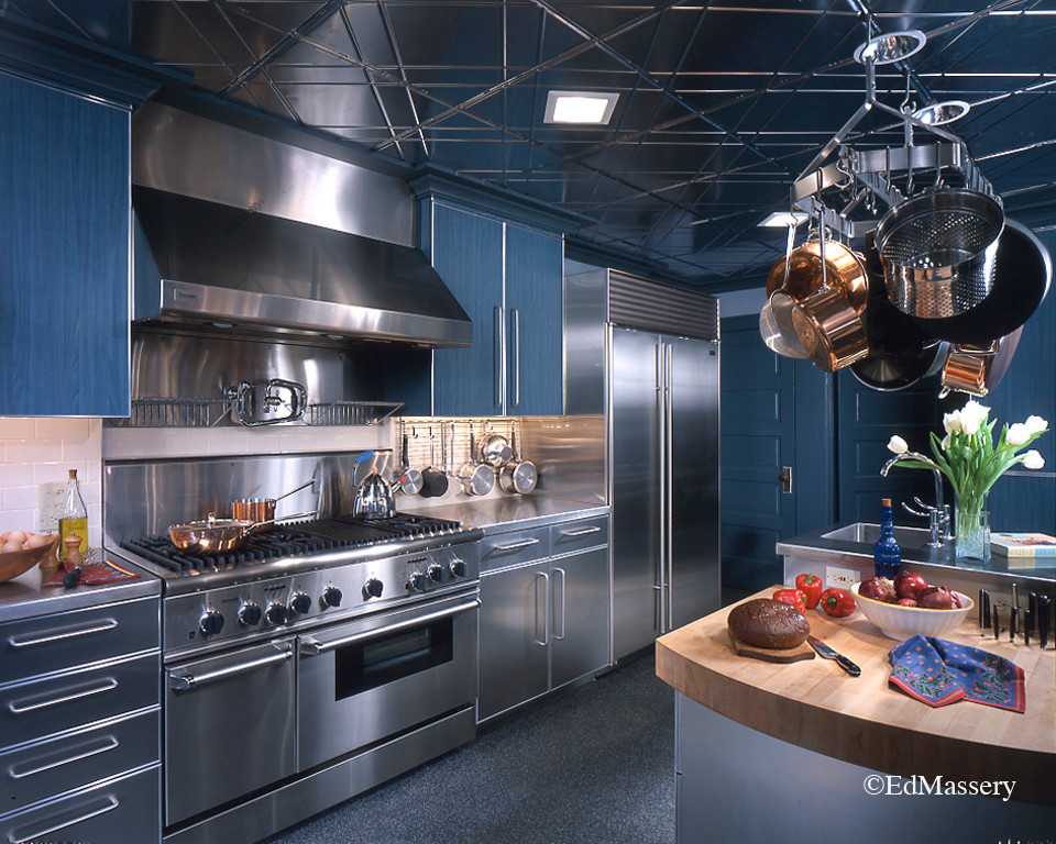 Example of a minimalist kitchen design with an integrated sink, flat-panel cabinets, stainless steel countertops, white backsplash, ceramic backsplash, stainless steel appliances and an island