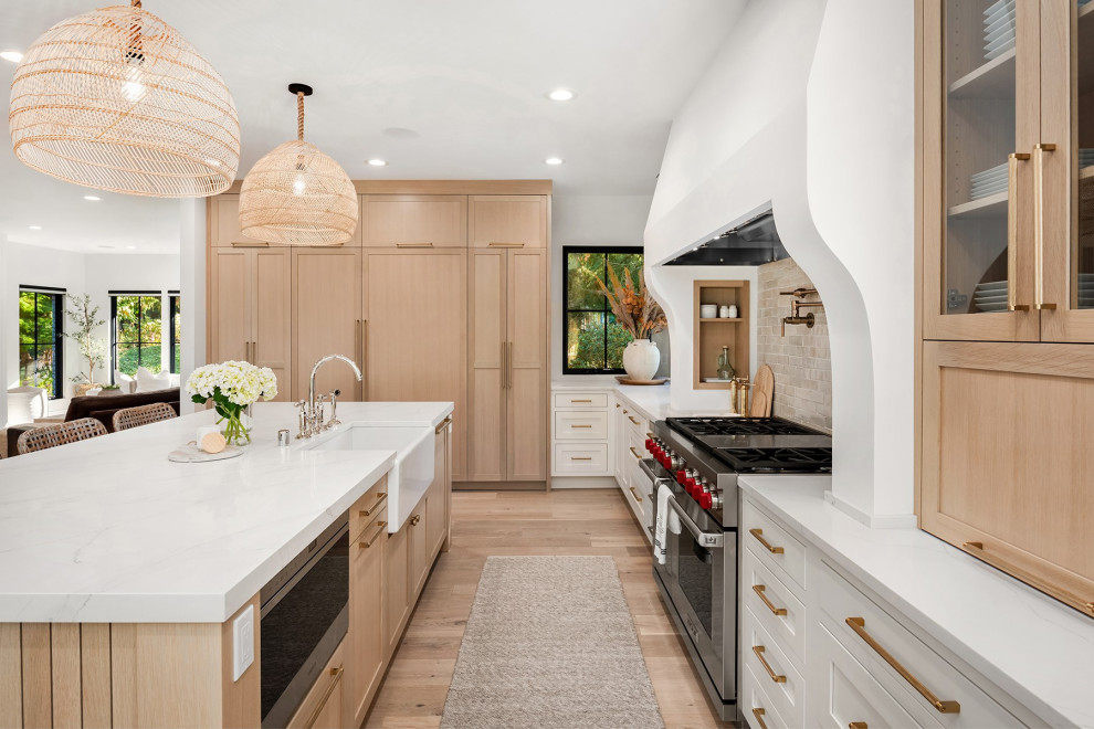 Design ideas for an expansive modern l-shaped eat-in kitchen in Seattle with a farmhouse sink, recessed-panel cabinets, light wood cabinets, marble benchtops, beige splashback, brick splashback, stainless steel appliances, light hardwood floors, with island, multi-coloured floor, white benchtop and vaulted.
