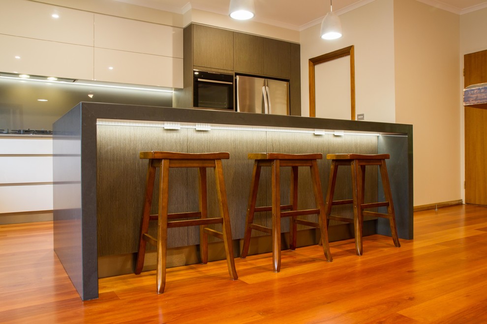 Large modern l-shaped eat-in kitchen in Melbourne with flat-panel cabinets, quartz benchtops, metallic splashback, glass sheet splashback, medium hardwood floors and with island.