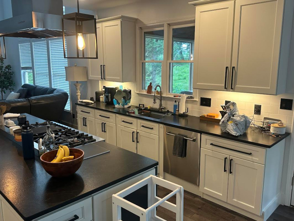Bright modern kitchen with white cabinets, black countertops, a large island, pendant lights, and windows above the sink.