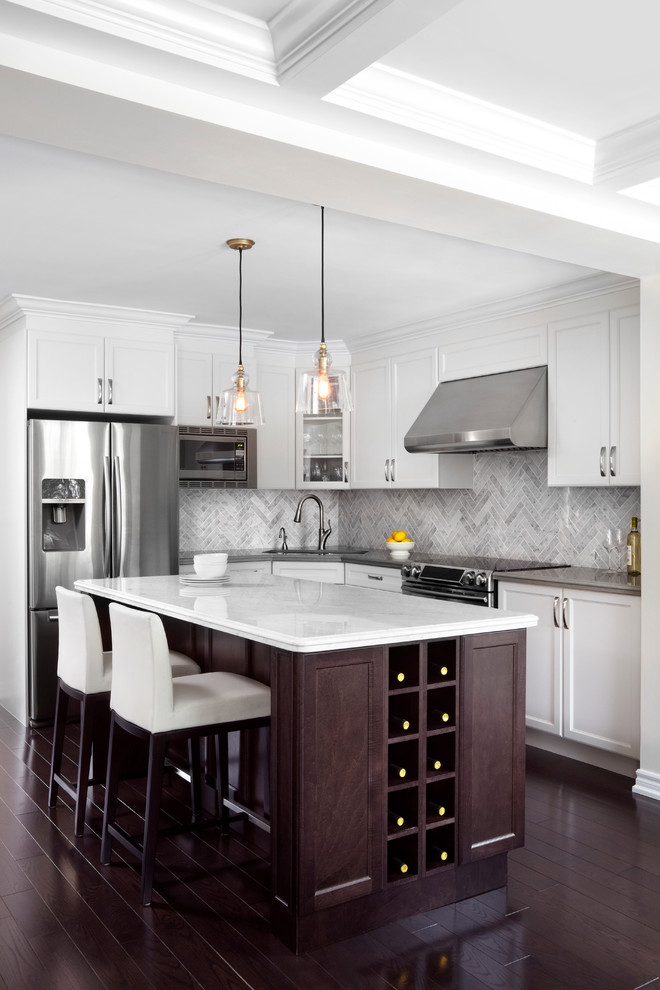 Inspiration for a mid-sized traditional l-shaped kitchen in Toronto with recessed-panel cabinets, white cabinets, solid surface benchtops, stone tile splashback, stainless steel appliances, dark hardwood floors, with island and grey splashback.
