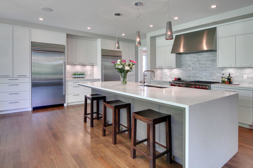 Example of a transitional medium tone wood floor and brown floor kitchen design in Calgary with an undermount sink, flat-panel cabinets, quartz countertops, gray backsplash, marble backsplash, stainless steel appliances and an island