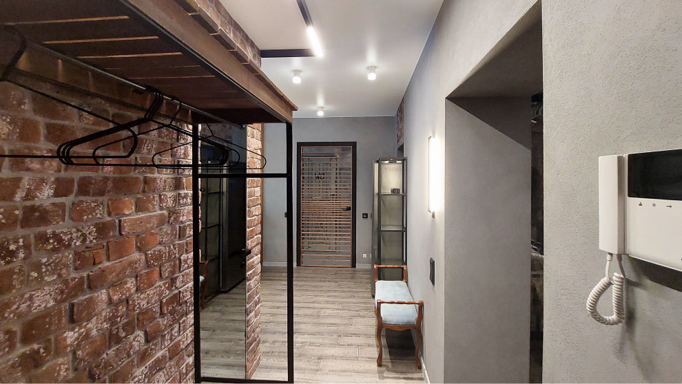 Идея дизайна: большая узкая прихожая: освещение в стиле лофт с паркетным полом среднего тона, коричневым полом, серыми стенами, одностворчатой входной дверью, серой входной дверью и кирпичными стенами