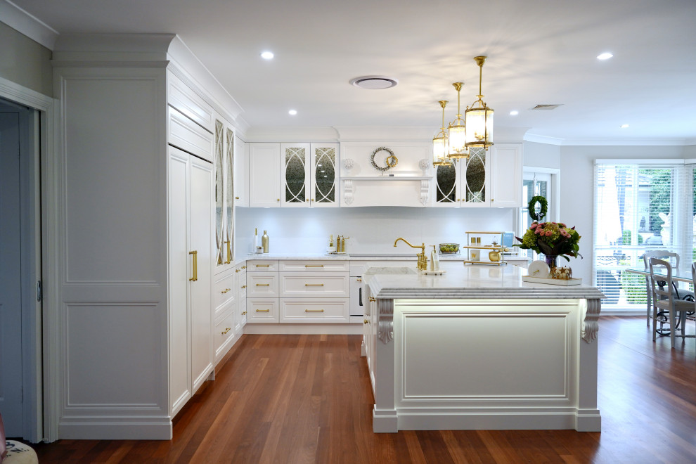 Inspiration för stora klassiska grått kök, med en rustik diskho, luckor med infälld panel, vita skåp, marmorbänkskiva, vitt stänkskydd, stänkskydd i keramik, vita vitvaror, mellanmörkt trägolv, en köksö och brunt golv