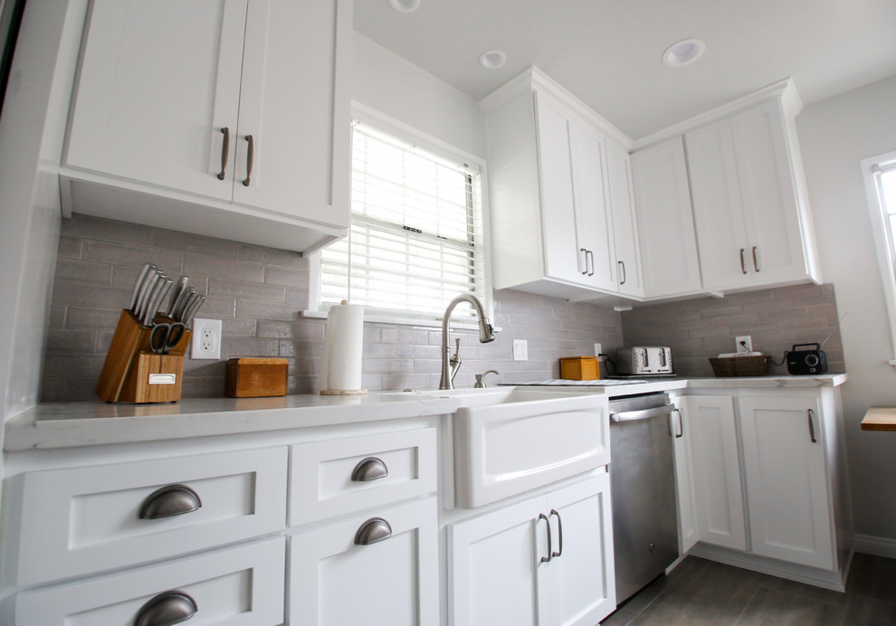 Design ideas for a mid-sized transitional l-shaped kitchen in Los Angeles with a farmhouse sink, shaker cabinets, white cabinets, quartzite benchtops, grey splashback, subway tile splashback, stainless steel appliances, light hardwood floors, no island, grey floor and white benchtop.