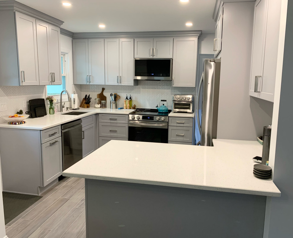 Photo of a mid-sized modern kitchen in New York with a drop-in sink, grey cabinets, quartz benchtops, grey splashback, glass tile splashback, stainless steel appliances, porcelain floors, grey floor and white benchtop.