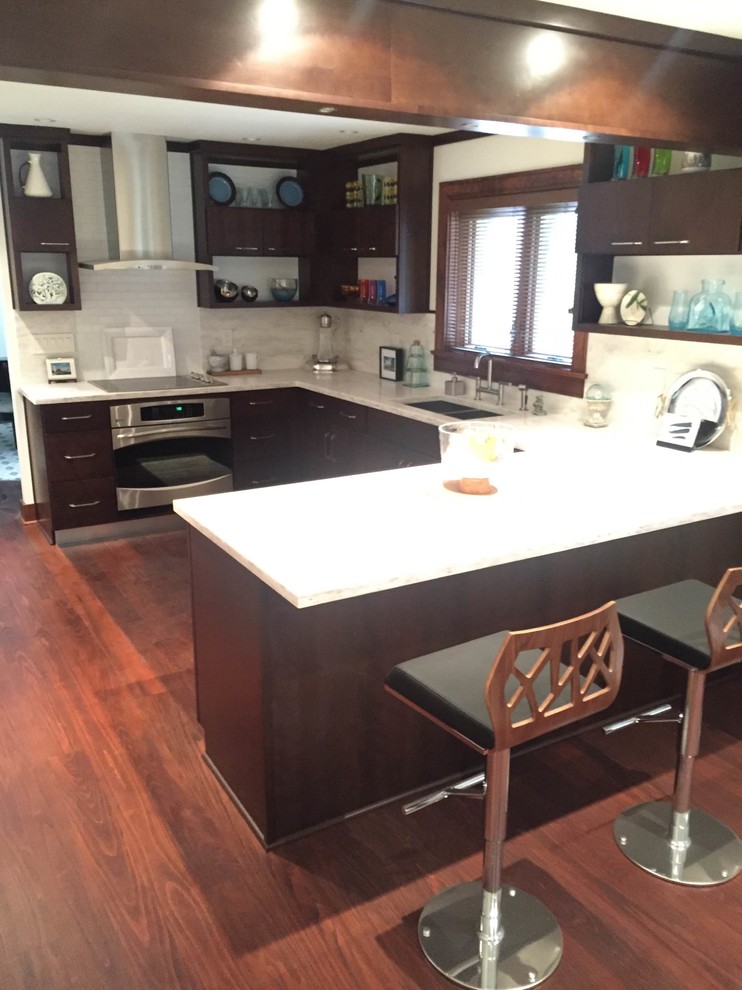 Example of a mid-sized transitional u-shaped medium tone wood floor and brown floor kitchen design with an undermount sink, flat-panel cabinets, dark wood cabinets, quartz countertops, gray backsplash, subway tile backsplash, stainless steel appliances and a peninsula