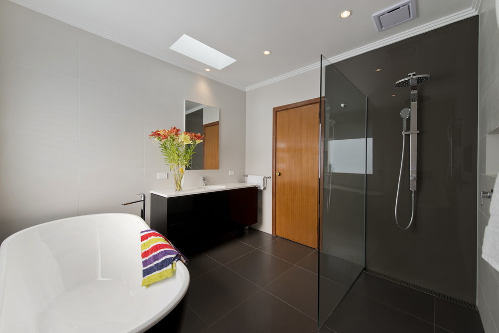 Mid-sized modern bathroom in Melbourne with flat-panel cabinets, black cabinets, a freestanding tub, an open shower, a wall-mount toilet, multi-coloured tile, porcelain tile, white walls, porcelain floors, an integrated sink, solid surface benchtops, grey floor and an open shower.