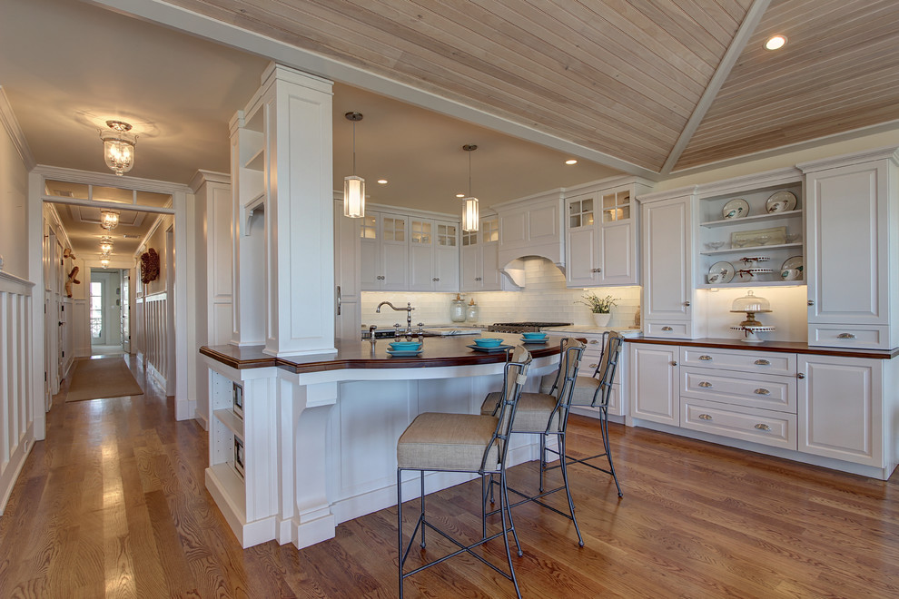 This is an example of a large beach style kitchen in Philadelphia with raised-panel cabinets, white cabinets, glass benchtops, white splashback, glass tile splashback, medium hardwood floors and with island.