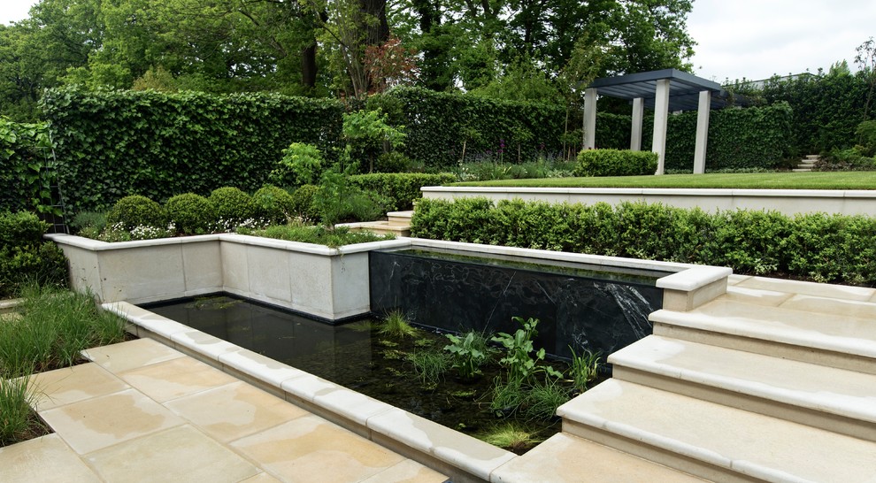 Photo of a large transitional backyard formal garden in London with with pond and natural stone pavers.