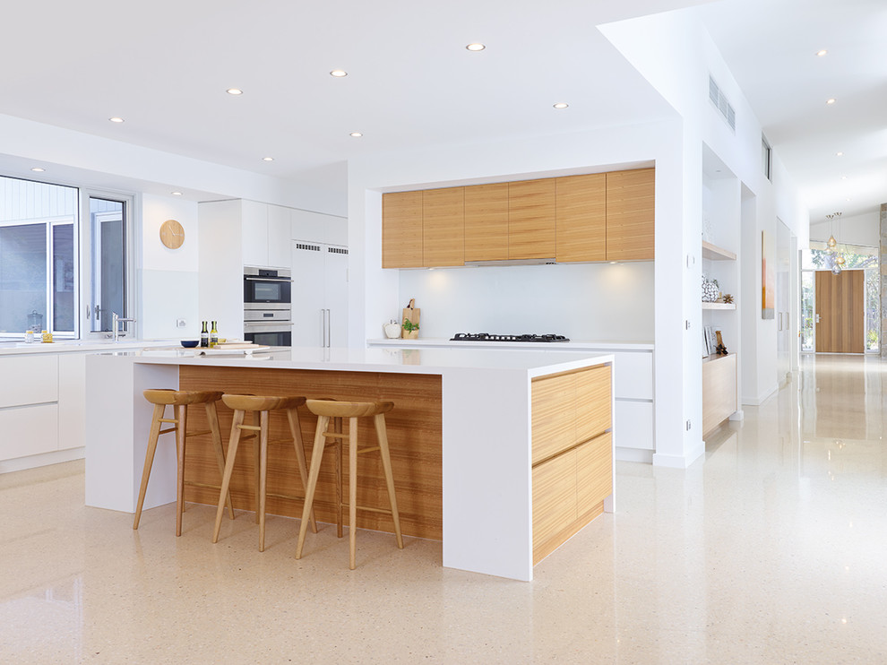Mid-sized contemporary l-shaped kitchen in Melbourne with a drop-in sink, marble benchtops, white splashback, glass sheet splashback, stainless steel appliances, concrete floors, with island, flat-panel cabinets and medium wood cabinets.