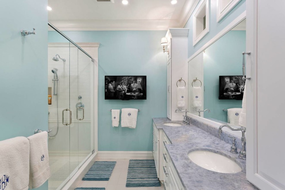 Design ideas for a mid-sized beach style master bathroom in Miami with raised-panel cabinets, white cabinets, a corner shower, a one-piece toilet, white tile, subway tile, blue walls, ceramic floors, an undermount sink, marble benchtops, beige floor, a hinged shower door and blue benchtops.