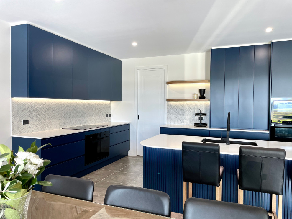 Large modern l-shaped open plan kitchen in Sydney with a drop-in sink, flat-panel cabinets, blue cabinets, quartz benchtops, grey splashback, marble splashback, black appliances, ceramic floors, with island, grey floor and white benchtop.