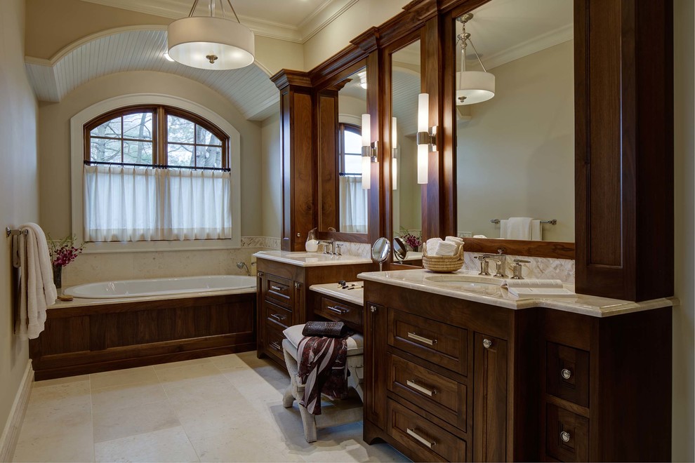 Design ideas for a large traditional master bathroom in New York with recessed-panel cabinets, dark wood cabinets, a drop-in tub, an alcove shower, beige tile, beige walls, travertine floors, an undermount sink, marble benchtops, beige floor and a hinged shower door.