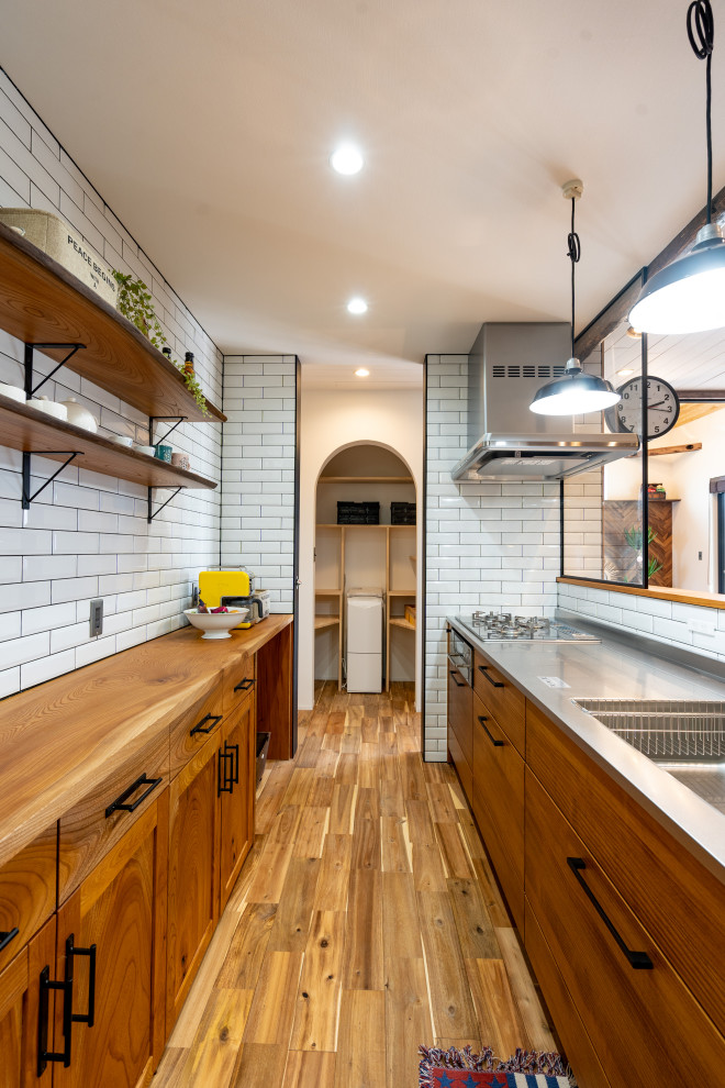 Inspiration for a single-wall open plan kitchen in Other with a single-bowl sink, beaded inset cabinets, distressed cabinets, stainless steel benchtops, white splashback, subway tile splashback, stainless steel appliances, with island, brown floor, brown benchtop and wallpaper.
