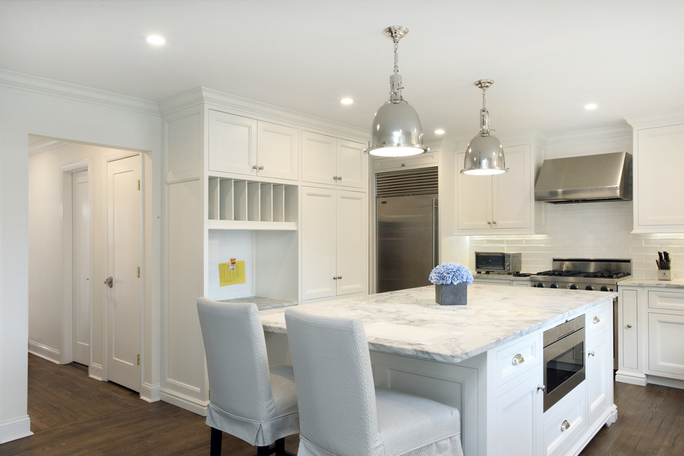 This is an example of a large contemporary l-shaped separate kitchen in New York with a farmhouse sink, recessed-panel cabinets, white cabinets, marble benchtops, white splashback, subway tile splashback, stainless steel appliances, medium hardwood floors and with island.